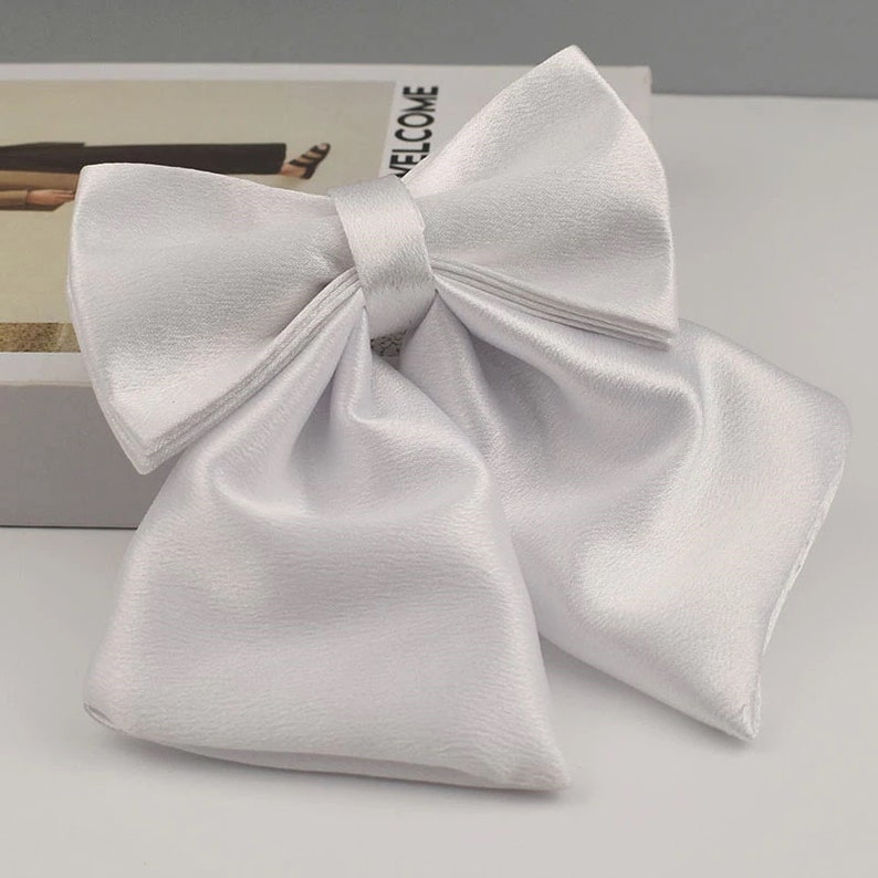 May include: A white satin bow tie with a large, full bow. The bow tie is made of a soft, luxurious fabric and has a classic, elegant design.