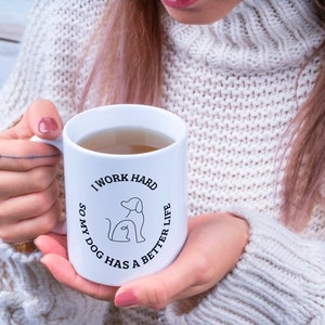 May include: White ceramic mug with black text that reads "I work hard so my dog has a better life". The text is in a circle with a dog and cat inside the circle.