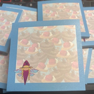 May include: A blue sticky note with a light blue border. The note has a pattern of pink and brown circles on a white background. A cartoon fairy with pink wings and a red hat is in the lower left corner of the note.