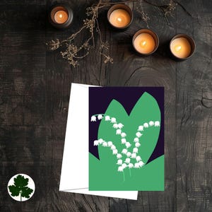 以下が含まれることがあります： 濃い青色の背景に、緑の葉の上に白い鈴蘭の花のイラストが描かれたグリーティングカード。カードの内側は空白で、白い封筒が付属しています。