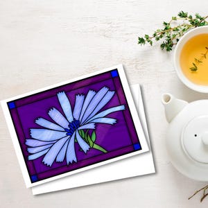 以下が含まれることがあります： 紫色の背景に青い花が描かれたグリーティングカード。濃い紫色の縁取りと青い角のアクセントが施されています。カードは白い表面に置かれ、白いティーポットと、タイムの小枝が入ったお茶のカップの隣にあります。