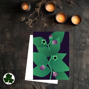 以下が含まれることがあります： 緑の葉、紫の花、黒い実の植物の植物画が描かれたグリーティングカード。カードは、暗い木製の表面に置かれ、ろうそくが灯され、小さな葉のステッカーが付いています。