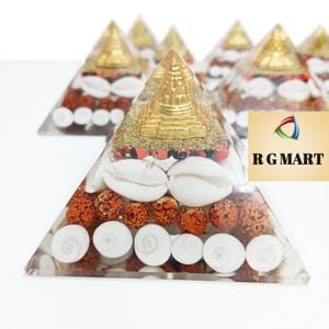 May include: A clear pyramid made of resin with a gold-colored miniature pagoda on top. The pyramid is filled with red beads, white seashells, and gold glitter.