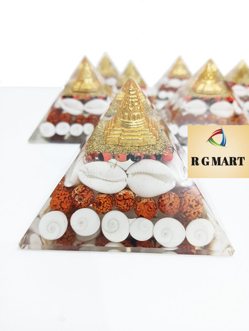 May include: A clear pyramid made of resin with a gold-colored miniature pagoda on top. The pyramid is filled with red beads, white seashells, and gold glitter.