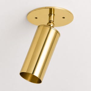 May include: A polished brass spotlight fixture featuring a cylindrical head attached to a circular ceiling mount. The design includes a swivel joint that allows for directional adjustment, showcasing a reflective metallic finish throughout the unit.