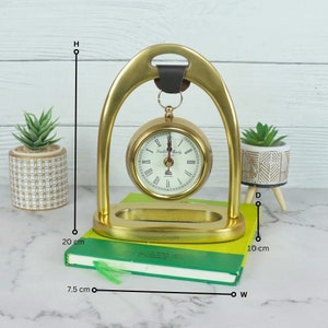 Peut inclure: Horloge dorée avec des chiffres romains sur un support en laiton avec une sangle en cuir. L'horloge mesure 10 cm de diamètre et le support 20 cm de haut.