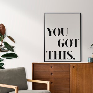 May include: A black and white motivational poster with the text "YOU GOT THIS." The poster is framed in a black frame and is hanging on a white wall.