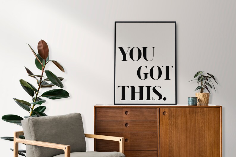 May include: A black and white motivational poster with the text "YOU GOT THIS." The poster is framed in a black frame and is hanging on a white wall.