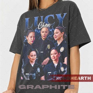 May include: Dark gray t-shirt featuring a graphic of five women in police uniforms with the text "LUCY Chen" in blue. The design includes lightning bolt accents and the words "STRONG HEARTH GRAPHITE".