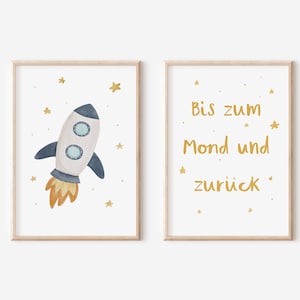 May include: Two framed prints with a white background and gold text. The left print features a blue and white rocket ship with orange flames. The right print says "Bis zum Mond und zurück".