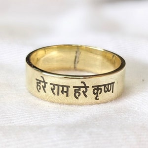 May include: A gold band ring with the inscription "Hare Ram Hare Krishna" in black lettering.