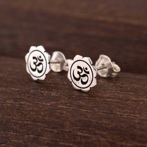 May include: A pair of silver earrings with a circular design featuring the Om symbol in black.