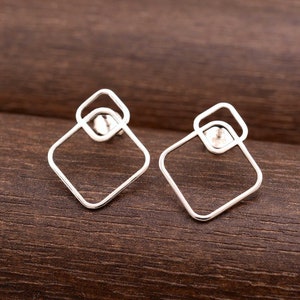 May include: A pair of silver geometric earrings with a square shape and a smaller square inside. The earrings are simple and modern.