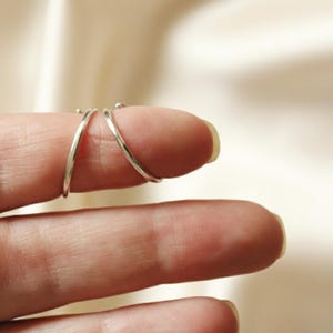 Puede incluir: Primer plano de tres anillos finos de plata. Los anillos se llevan en un dedo, con dos anillos cruz&aacute;ndose. Los anillos son sencillos y elegantes, con un acabado pulido. Los anillos probablemente est&aacute;n hechos de plata de ley o un metal similar.