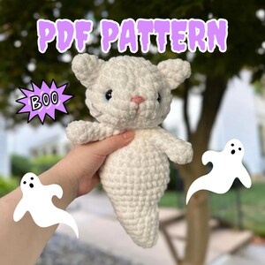 Op de afbeelding: Een wit gehaakt spookkat amigurumi patroon. Het patroon bevat instructies voor het haken van een spookkat met een wit lichaam en een roze neus. Het patroon is beschikbaar als PDF-download. De afbeelding bevat ook de tekst "PDF PATTERN" en "BOO!" in een paarse spraakballon.