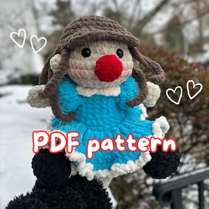 Op de afbeelding: Haakpoppenpatroon PDF. De pop draagt een blauwe jurk met witte versiering en een bruine hoed. De pop heeft een rode neus en roze wangen.