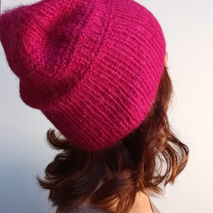 Könnte beinhalten: Eine rosafarbene Strickmütze mit einem lockeren Sitz. Die Mütze ist aus einem weichen, flauschigen Garn gefertigt.