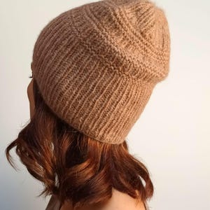 Könnte beinhalten: Eine braune Strickmütze mit einem lockeren Sitz. Die Mütze ist aus einem weichen, warmen Material gefertigt und perfekt für kaltes Wetter.