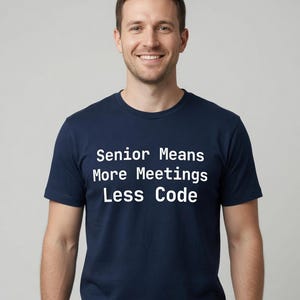 May include: A navy blue short-sleeved t-shirt featuring the white text Senior Means More Meetings Less Code printed in a clean sans-serif font across the chest. The garment has a classic crew neckline and a standard fit for everyday wear.
