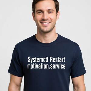 Puede incluir: Camiseta azul marino con el texto blanco "Systemctl Restart motivation.service". La camiseta es de cuello redondo y la lleva puesta una persona.
