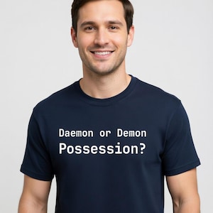 May include: A navy blue t-shirt with the text "Daemon or Demon Possession?" in white. The shirt is a crew neck style and is being worn by a person.