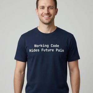 Op de afbeelding: Een marineblauw t-shirt met korte mouwen en de witte tekst "Working Code Hides Future Pain" op de borst gedrukt. Het kledingstuk heeft een klassieke ronde hals en een standaard pasvorm, gemaakt van een effen gekleurde stof.