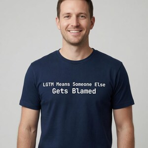 May include: A navy blue short-sleeved t-shirt featuring white text printed on the chest that reads: LGTM Means Someone Else Gets Blamed. The shirt has a crew neckline and a standard fit, constructed from a solid-coloured fabric.