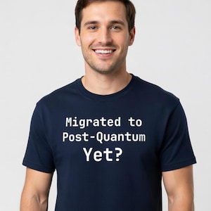 May include: A navy blue t-shirt with the white text "Migrated to Post-Quantum Yet?". The t-shirt has a crew neck and is made of a soft material. The person wearing the shirt is smiling.