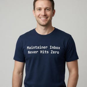 May include: A navy blue short-sleeved t-shirt featuring the white text "Maintainer Inbox Never Hits Zero" printed across the chest. The garment has a classic crew neckline and a standard fit, providing a clean and straightforward appearance.