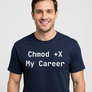 May include: Navy blue t-shirt with the text "Chmod +X My Career" in white. The shirt is a crew neck style and appears to be made of a soft material. The person in the image is smiling.