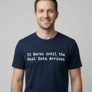 以下が含まれることがあります： 胸元に白い文字で「It Works Until the Real Data Arrives」とプリントされた、ネイビーブルーの半袖Tシャツ。この衣類は、クラシックなクルーネックと、日常着に適したシンプルでクリーンなデザインが特徴です。