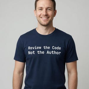 May include: A navy blue short-sleeved t-shirt featuring the white text "Review the Code Not the Author" printed across the chest. The garment has a classic crew neckline and a standard fit, providing a clean and straightforward appearance.