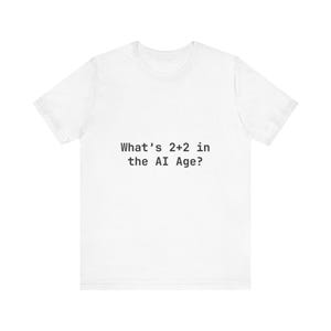 Op de afbeelding: Wit T-shirt met de zwarte tekst: "What's 2+2 in the AI Age?" Het T-shirt heeft een ronde hals en korte mouwen.
