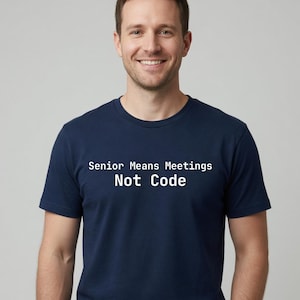 May include: A navy blue short-sleeved t-shirt featuring the white text "Senior Means Meetings Not Code" printed across the chest. The shirt has a classic crew neckline and a simple, clean design, providing a straightforward look for daily wear.