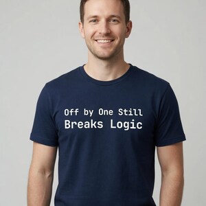 Könnte beinhalten: Ein dunkelblaues T-Shirt mit kurzen Ärmeln und dem weißen Schriftzug "Off by One Still Breaks Logic" auf der Brust. Das Kleidungsstück hat einen klassischen Rundhalsausschnitt und einen geraden Saum, was für einen schlichten Look sorgt.