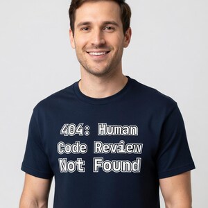 May include: A navy blue t-shirt with the text "404: Human Code Review Not Found" in white block letters. The shirt is being worn by a person smiling at the camera.