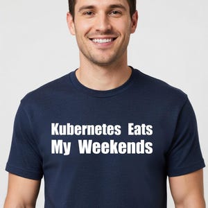 Puede incluir: Una camiseta azul marino con el texto blanco "Kubernetes Eats My Weekends". La camiseta está hecha de un material suave y es adecuada para ropa casual. La persona de la imagen está sonriendo.