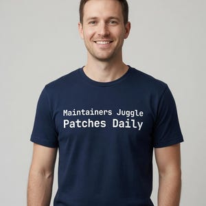 May include: A navy blue short-sleeved t-shirt featuring the white text "Maintainers Juggle Patches Daily" printed in a clean, sans-serif font across the chest area. The garment has a classic crew neckline and a standard, straight-cut fit.