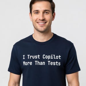 Puede incluir: Una camiseta azul marino con el texto blanco "I Trust Copilot More Than Tests". La camiseta de manga corta la lleva una persona sonriendo. El fondo es blanco liso.