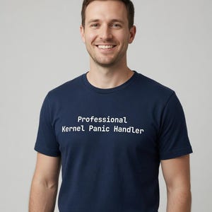Puede incluir: Una camiseta azul marino de manga corta con el texto blanco Professional Kernel Panic Handler impreso en una fuente estilo máquina de escribir en el pecho. La prenda tiene un cuello redondo clásico y un diseño sencillo y limpio.