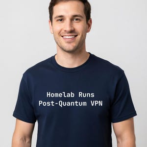 May include: A navy blue t-shirt with the text "HomeLab Runs Post-Quantum VPN" in white. The t-shirt is being worn by a person with short brown hair and a smile.