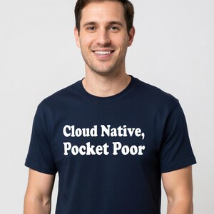May include: A navy blue t-shirt with the text "Cloud Native, Pocket Poor" in white. The shirt is a crew neck style and is being worn by a person.