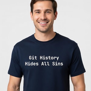 Puede incluir: Una camiseta azul marino con el texto blanco "Git History Hides All Sins". La camiseta la lleva una persona con pelo castaño corto y una sonrisa. El fondo es blanco liso.