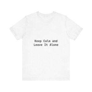 Puede incluir: Camiseta blanca con el texto "Keep Calm and Leave It Alone" impreso en negro. La camiseta tiene mangas cortas y cuello redondo. El texto está centrado en la parte delantera de la camiseta.