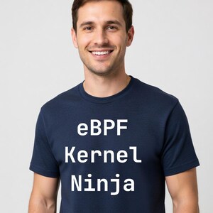 May include: Navy blue t-shirt with the text "eBPF Kernel Ninja" in white. The shirt is a crew neck style and is being worn by a person smiling at the camera. The background is a solid light gray.