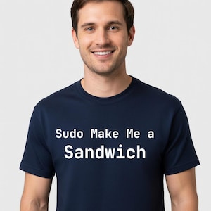 May include: A navy blue short-sleeved t-shirt featuring the white text "Sudo Make Me a Sandwich" printed across the chest. The garment has a classic crew neckline and a standard fit, showcasing a clean design with bold, sans-serif lettering.