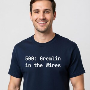 May include: Navy blue t-shirt with the text "500: Gremlin in the Wires" in white. The shirt is a crew neck style and is being worn by a person.