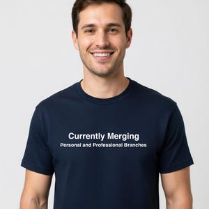 May include: A navy blue t-shirt with the text "Currently Merging Personal and Professional Branches" in white. The shirt is a crew neck style and is being worn by a person.