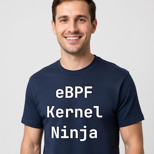 May include: Navy blue t-shirt with the text "eBPF Kernel Ninja" in white. The shirt is a crew neck style and is being worn by a person smiling at the camera. The background is a solid light gray.