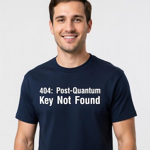 May include: A navy blue t-shirt with the text "404: Post-Quantum Key Not Found" in white. The shirt is worn by a smiling person.